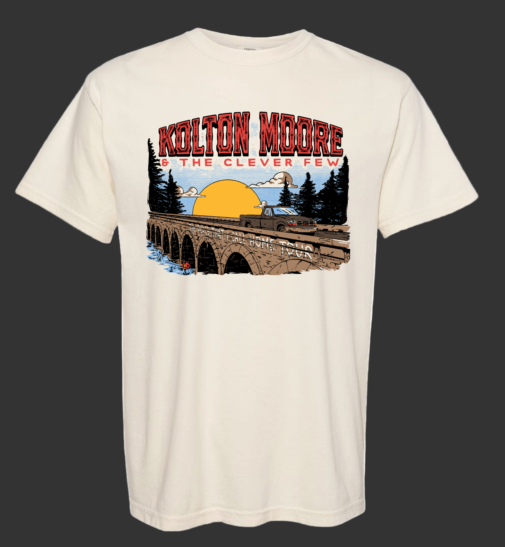 Beige t-shirt with a graphic design of a bridge, trees, and sunset, featuring the text 'Kolton Moore & The Clever Few'.